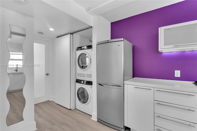 laundry room featuring stacked washer / drying machine and light hardwood / wood-style floors