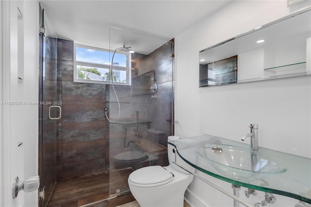 bathroom featuring toilet, a shower with shower door, and sink