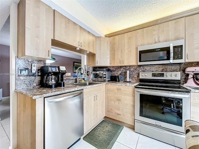 kitchen featuring light brown cabinetry, light tile patterned flooring, a textured ceiling, and appliances with stainless steel finishes