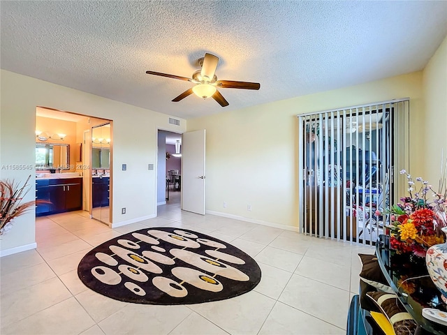 bedroom with ensuite bathroom, ceiling fan, light tile patterned floors, and a textured ceiling