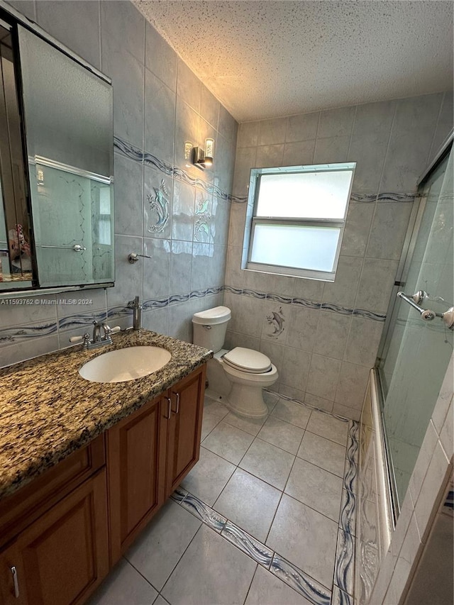 full bathroom with a textured ceiling, tile patterned floors, toilet, tile walls, and vanity