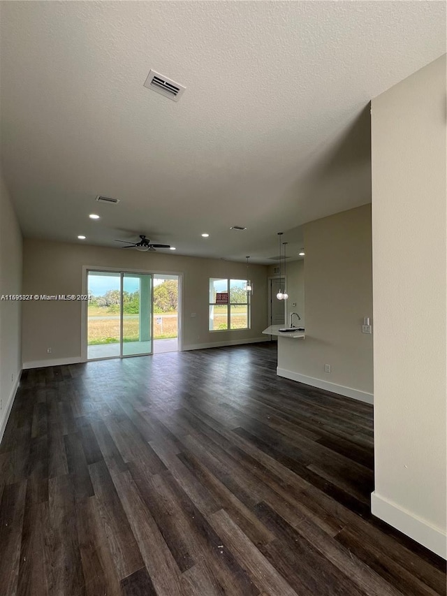 unfurnished living room with ceiling fan, dark wood-type flooring, and a textured ceiling