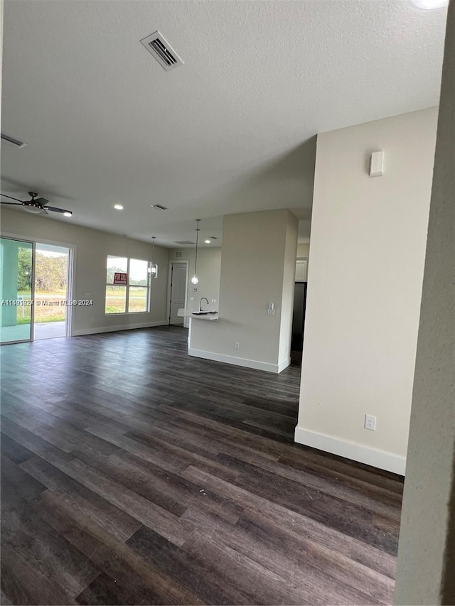 unfurnished living room featuring ceiling fan, dark hardwood / wood-style flooring, and a textured ceiling