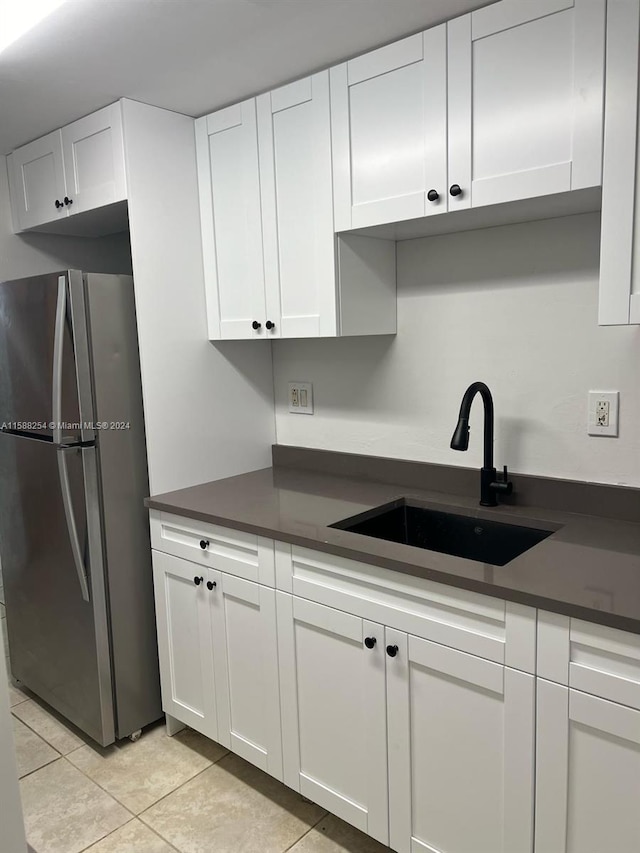 kitchen with light tile patterned floors, white cabinetry, stainless steel refrigerator, and sink