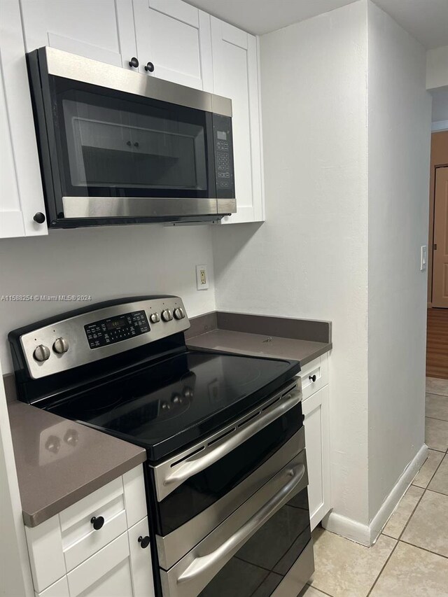 kitchen featuring appliances with stainless steel finishes, light tile patterned floors, and white cabinetry