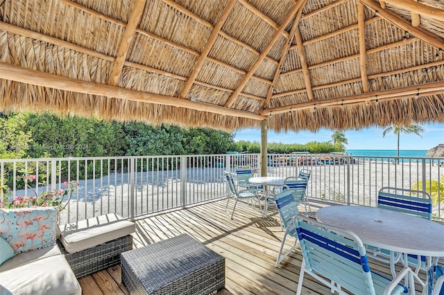 wooden terrace with outdoor dining space, a gazebo, a beach view, and a water view