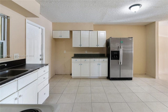 kitchen featuring sink, stainless steel refrigerator with ice dispenser, light tile patterned floors, a textured ceiling, and white cabinetry