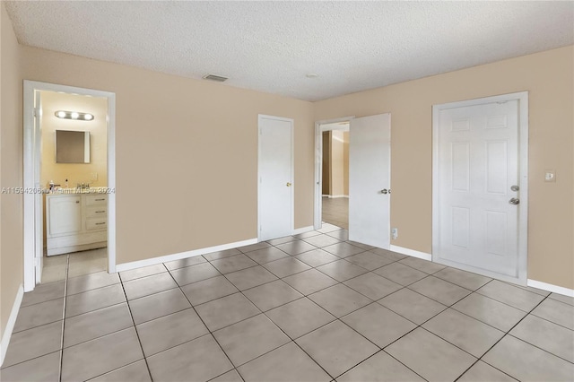 unfurnished bedroom featuring connected bathroom, light tile patterned floors, and a textured ceiling