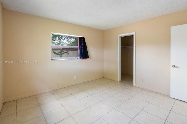 unfurnished bedroom featuring light tile patterned flooring, a walk in closet, a textured ceiling, and a closet