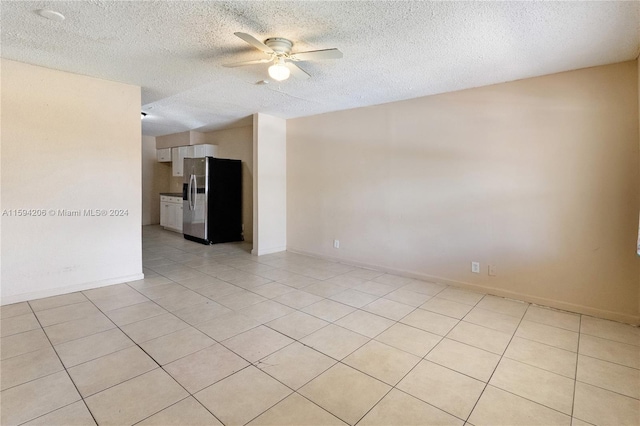 spare room featuring ceiling fan, light tile patterned floors, and a textured ceiling