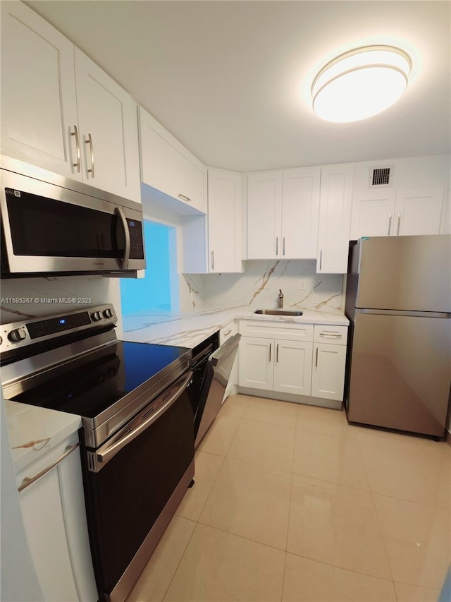 kitchen featuring sink, stainless steel appliances, white cabinets, light stone counters, and light tile patterned flooring