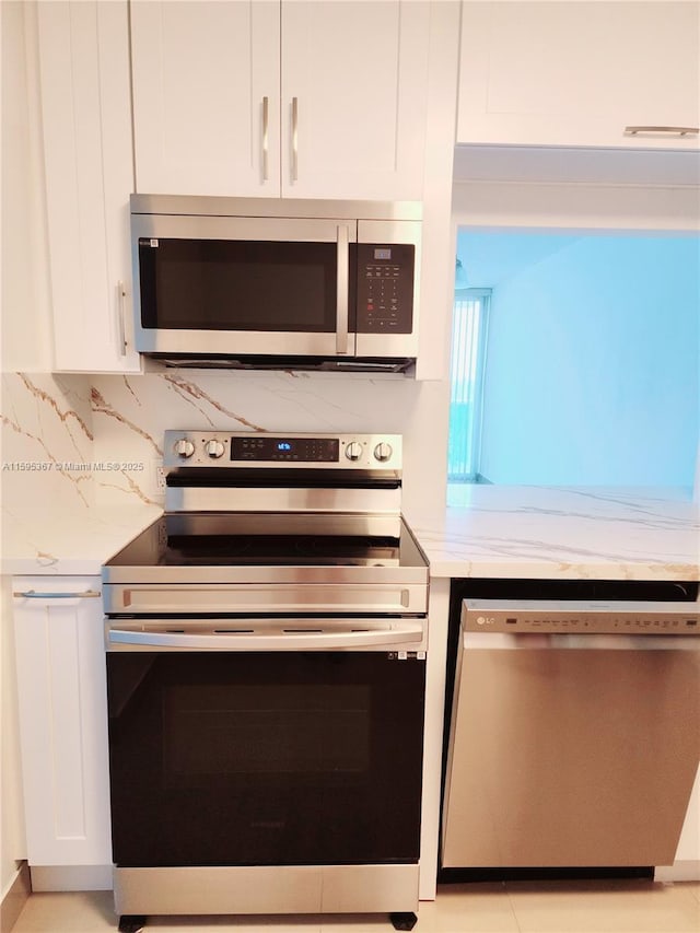 kitchen featuring white cabinets, appliances with stainless steel finishes, tasteful backsplash, and light stone countertops