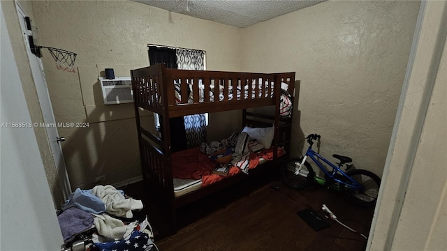 bedroom with a wall unit AC, a textured ceiling, and hardwood / wood-style flooring