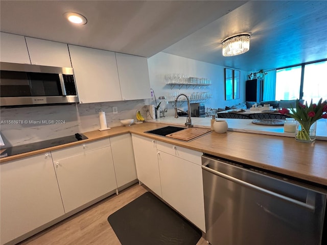 kitchen featuring stainless steel appliances, open floor plan, white cabinets, a sink, and light wood-type flooring