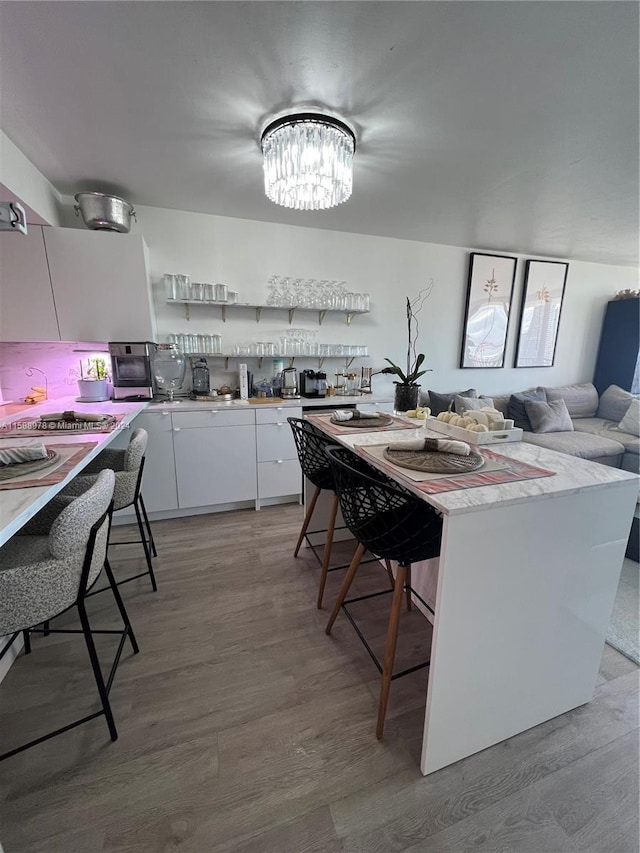 kitchen with light wood-style flooring, a breakfast bar area, white cabinetry, and backsplash