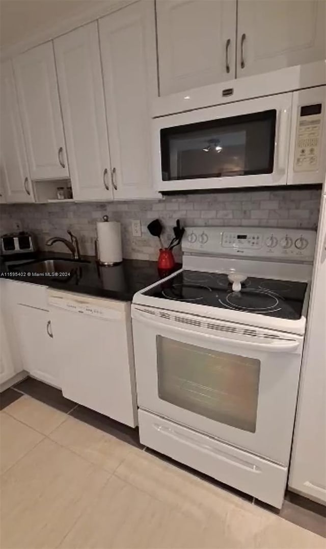 kitchen with white appliances, a sink, white cabinetry, backsplash, and dark countertops