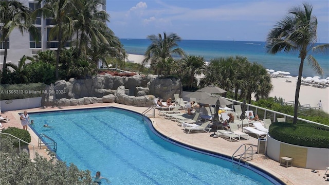 view of swimming pool with a patio area, a water view, and a view of the beach