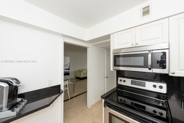 kitchen featuring white cabinets, appliances with stainless steel finishes, light tile patterned flooring, and dark stone countertops