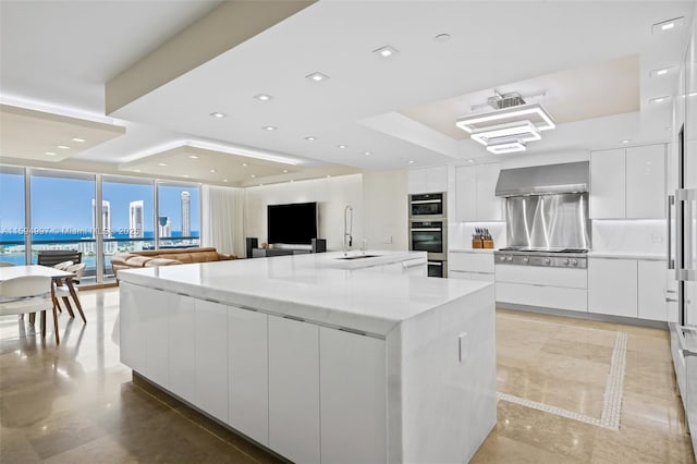 kitchen with sink, wall chimney exhaust hood, appliances with stainless steel finishes, a large island, and white cabinetry