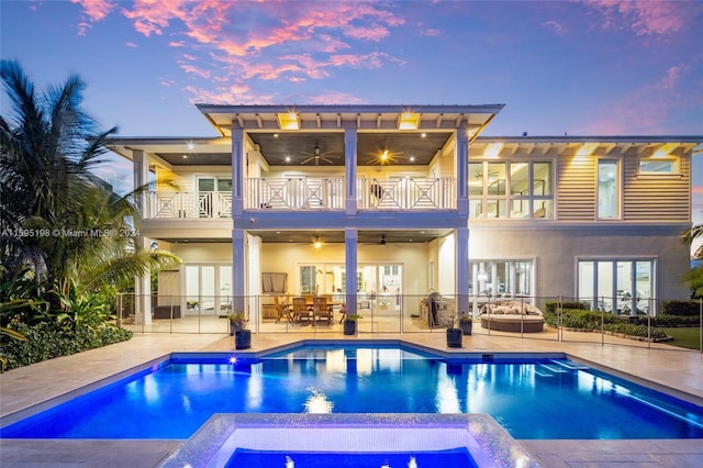 back house at dusk with a swimming pool with hot tub, a patio, a balcony, and ceiling fan