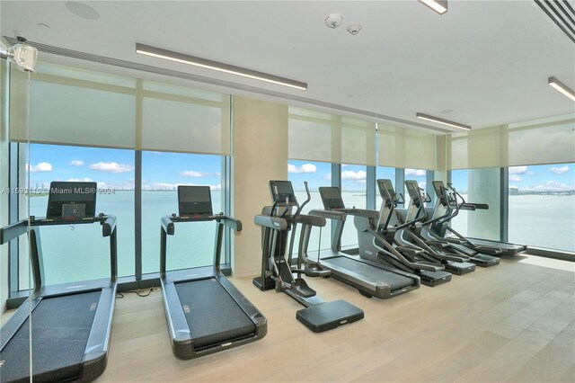 gym featuring hardwood / wood-style floors, a water view, and a wall of windows