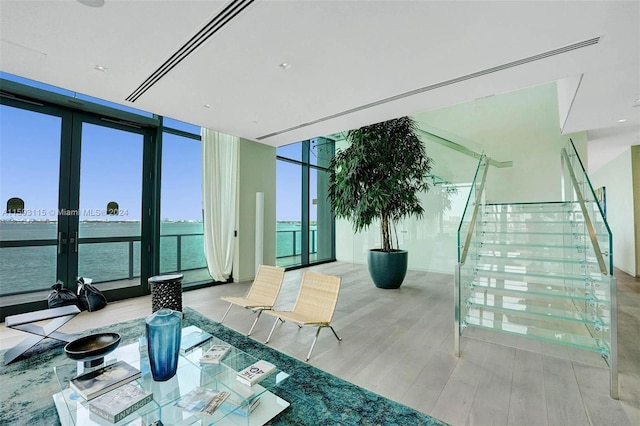 interior space featuring expansive windows, a water view, french doors, and light hardwood / wood-style flooring