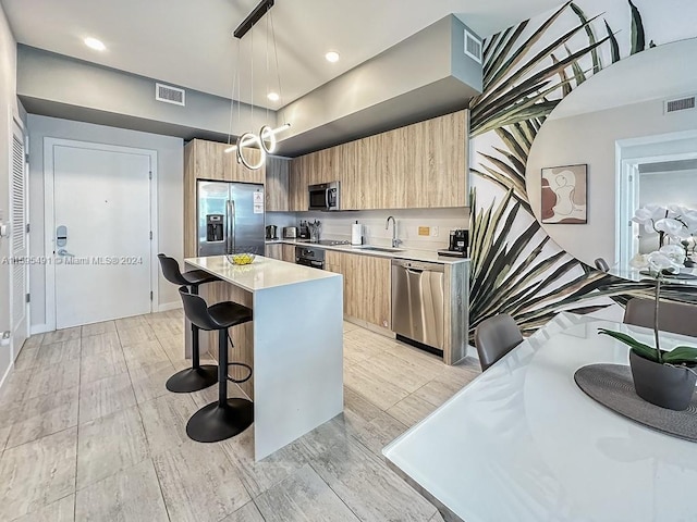 kitchen with a center island, hanging light fixtures, a kitchen bar, appliances with stainless steel finishes, and light wood-type flooring