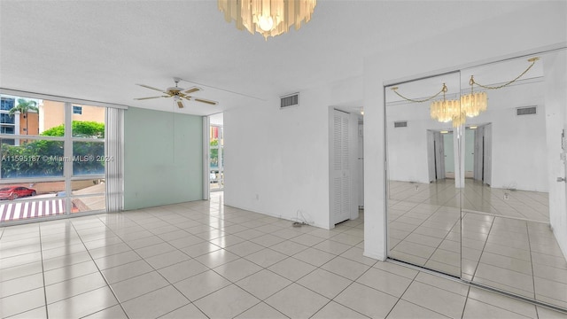 empty room featuring expansive windows, ceiling fan with notable chandelier, light tile patterned floors, and a textured ceiling