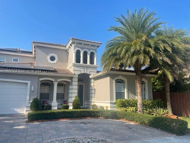 view of front facade with stucco siding, roof mounted solar panels, driveway, and fence