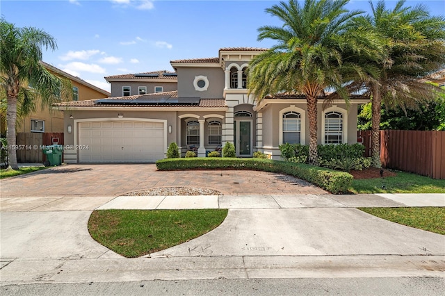 mediterranean / spanish house featuring decorative driveway, fence, a garage, stucco siding, and solar panels