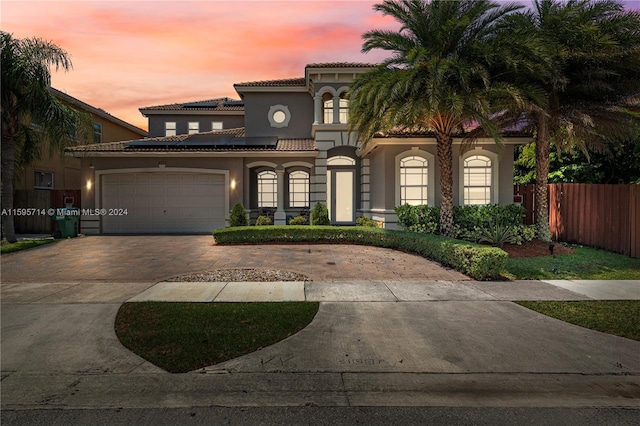 mediterranean / spanish-style house featuring a tiled roof, stucco siding, solar panels, decorative driveway, and a garage