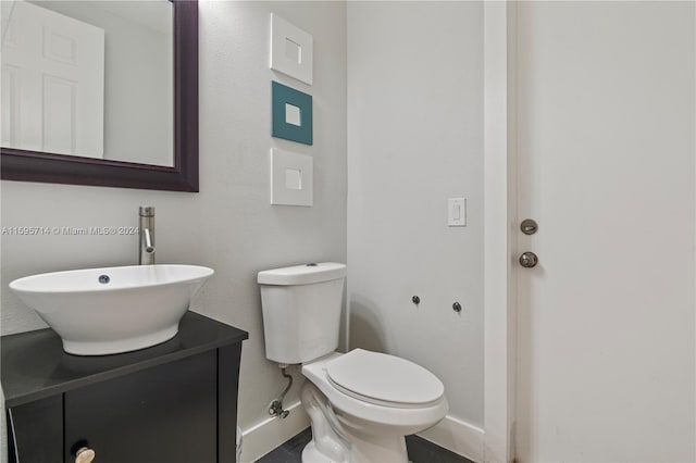 half bathroom with baseboards, toilet, and vanity