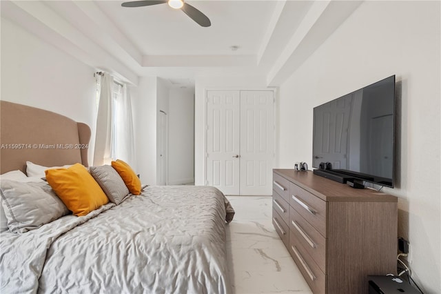 bedroom with a raised ceiling, marble finish floor, ceiling fan, and a closet