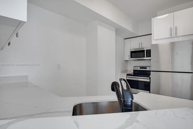 kitchen with stainless steel appliances, light stone counters, and white cabinetry