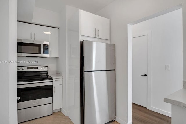 kitchen featuring light stone counters, appliances with stainless steel finishes, white cabinetry, and light hardwood / wood-style flooring