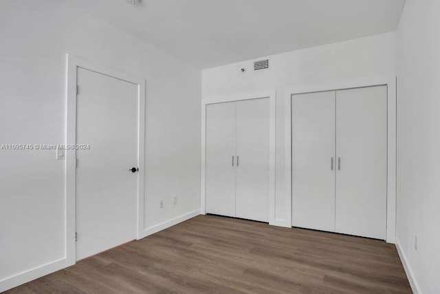 unfurnished bedroom with two closets and hardwood / wood-style floors