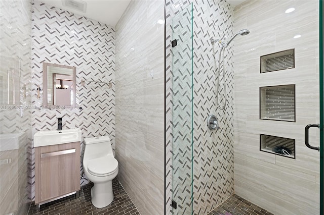 bathroom with tile patterned floors, toilet, a shower with shower door, vanity, and tile walls