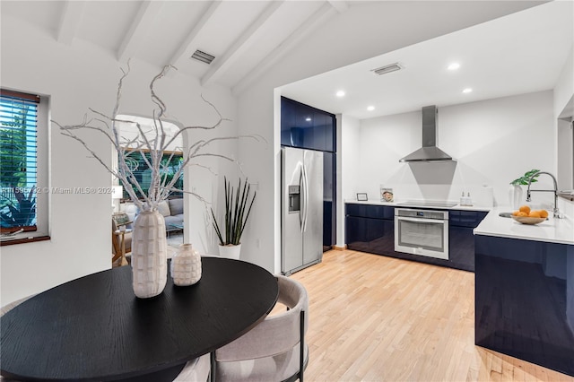 kitchen featuring vaulted ceiling with beams, sink, wall chimney exhaust hood, light hardwood / wood-style flooring, and stainless steel appliances