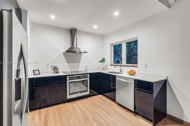 kitchen with stainless steel appliances, light wood-type flooring, sink, and wall chimney range hood