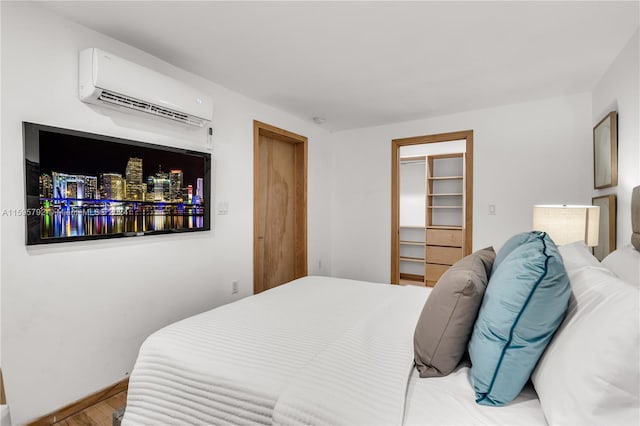 bedroom featuring an AC wall unit, light hardwood / wood-style flooring, a walk in closet, and a closet