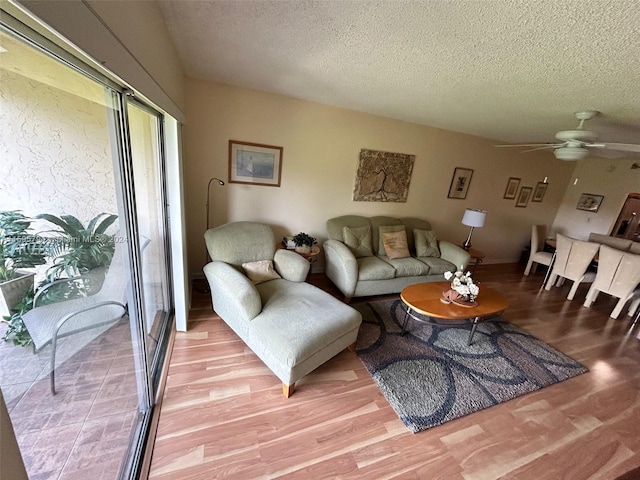 living room with ceiling fan, light wood-type flooring, and a textured ceiling