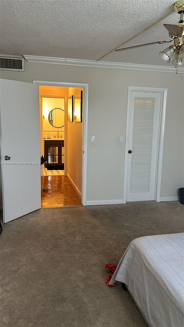 carpeted bedroom with a textured ceiling, ceiling fan, a fireplace, and crown molding