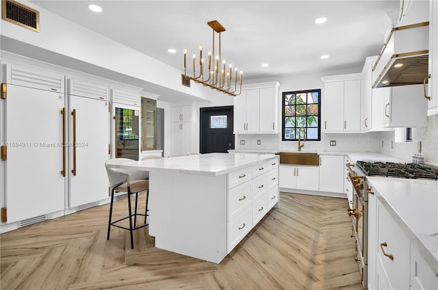 kitchen with sink, a kitchen island, light parquet floors, high quality appliances, and white cabinets