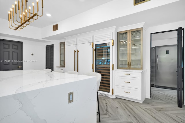 kitchen featuring light stone countertops, wine cooler, light parquet floors, decorative light fixtures, and white cabinets