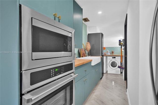 kitchen featuring decorative backsplash, appliances with stainless steel finishes, light parquet floors, butcher block countertops, and washer / clothes dryer