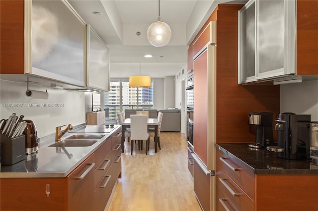 kitchen with decorative light fixtures, oven, light wood-type flooring, and sink