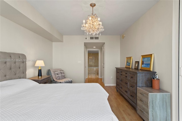 bedroom with connected bathroom, light hardwood / wood-style floors, and an inviting chandelier