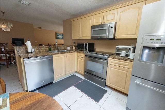 kitchen with a textured ceiling, appliances with stainless steel finishes, kitchen peninsula, light brown cabinets, and a chandelier