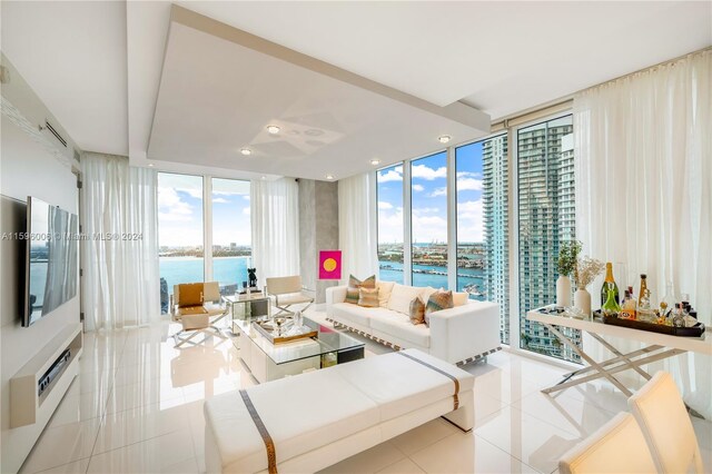 living room featuring a wealth of natural light, a water view, light tile floors, and a wall of windows