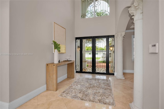 foyer featuring french doors, a high ceiling, light tile patterned floors, and decorative columns